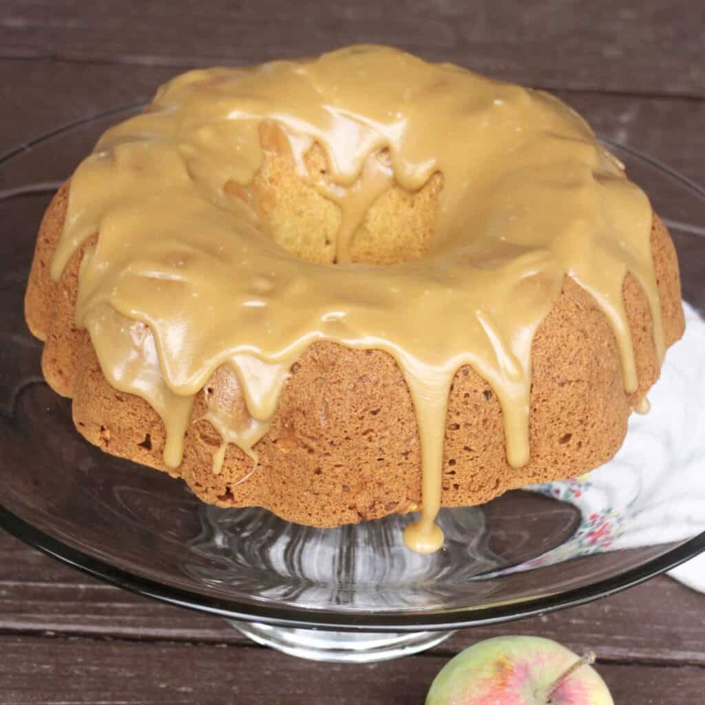 A caramel frosted apple bundt cake sits on a glass cake plate.