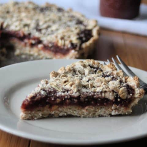 A slice of gluten-free jam tart on a plate with a fork.