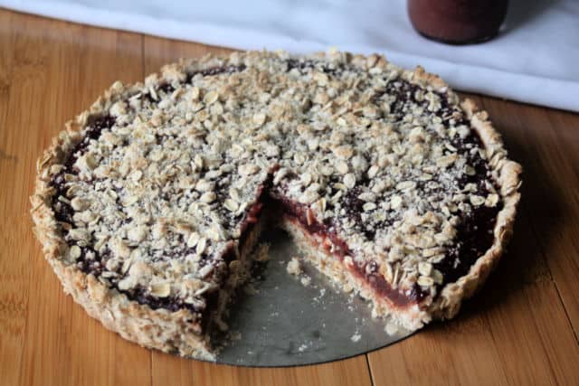 A gluten-free jam tart with piece missing on a table.