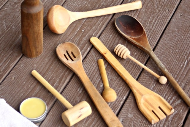 Wooden spoons sitting on a table with a tin of wood spoon oil and white cotton rag.