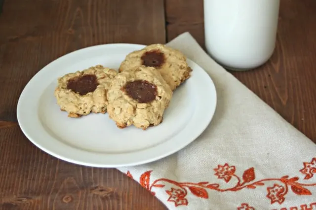 Peanut butter and jelly thumbprint cookies on a plate with a glass of milk