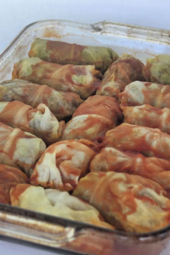 A glass baking tray full of cooked cabbage rolls covered in tomato juice.