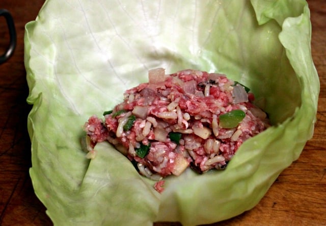 A cabbage leaf with a mixture of raw meat, rice, and vegetables inside.