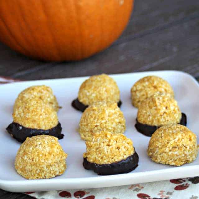 A white plate full of pumpkin macaroons with pumpkin in the background.