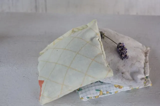 On herbal dream pillow leaning on a stack of 2 dream pillows topped with fresh lavender flower.