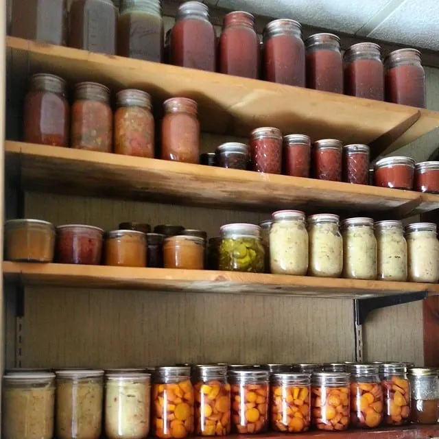 Jars of home canned items on wooden shelves.