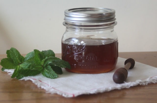 Mint infused honey in a jar on a white napkin with fresh mint and honey dipper