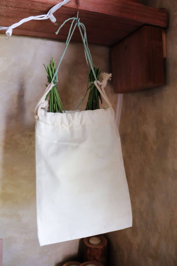 A canvas bag containing bundles of lavender stems hangs from a hook to dry. 