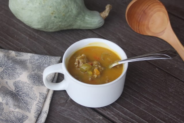 Hubbard squash sausage soup in a white cup with a spoon. 