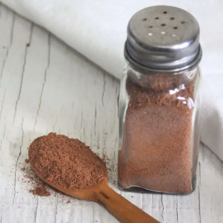 A wooden spoon full of ground flaxseed and spices sitting next to a salt shaker full of the same mixture.