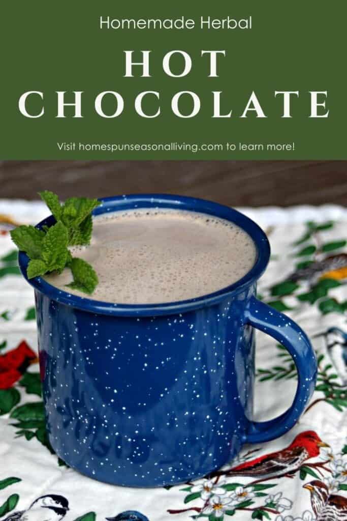 A blue tin cup full of hot chocolate decorated with fresh sprigs of mint sitting on a floral and bird covered placemat with text overlay stating: homemade herbal hot chocolate.