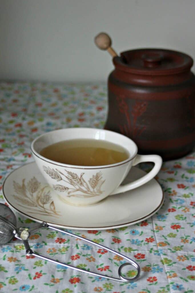 A cup of mint tea sits on a saucer. Behind the cup is a honey jar. 