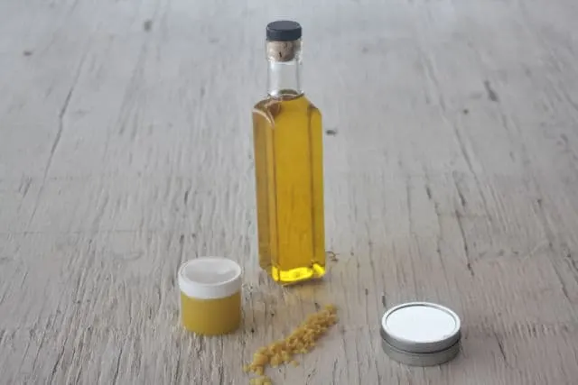 Strained dandelion oil in a clear bottle surrounded by containers of balms and beeswax.