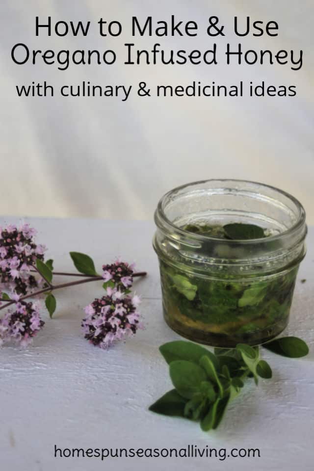 A jar of oregano leaves infusing with honey with a stem of oregano flowers sitting next to it on a table.