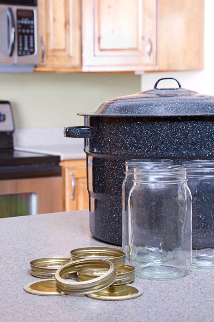A water bath canner sits on the counter with empty canning jars, canning rings, and canning lids.