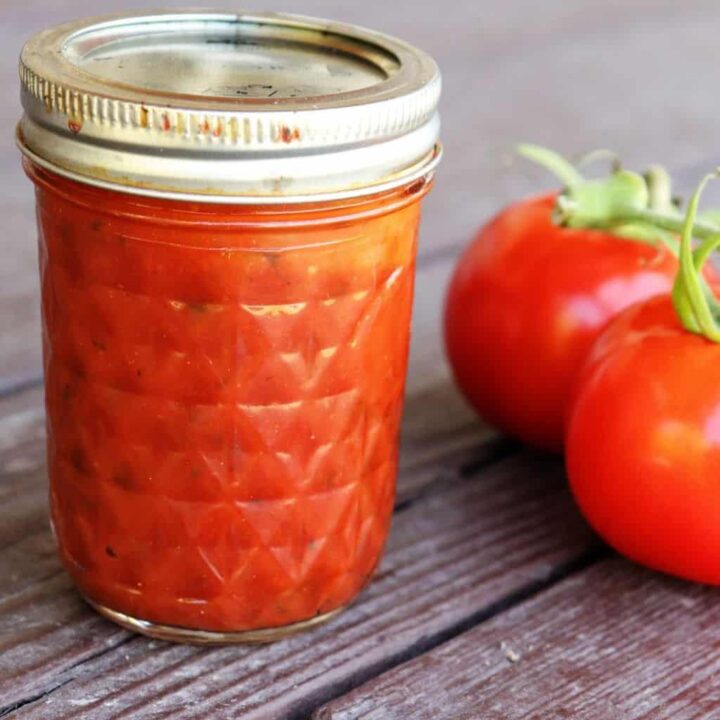 A jar of pizza sauce sitting next to fresh tomatoes.