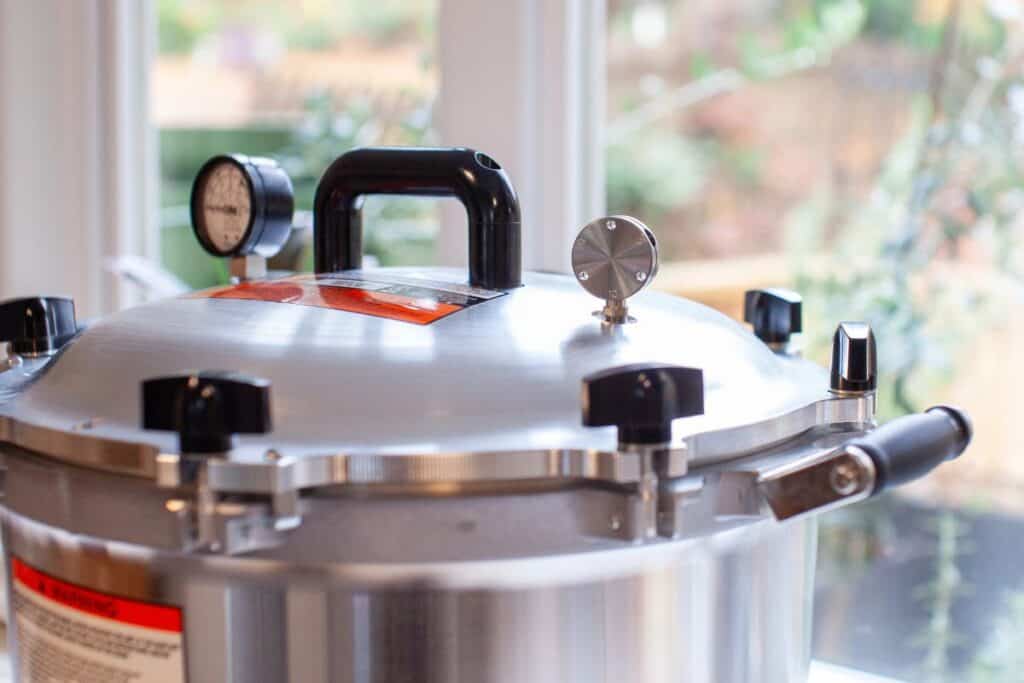 A pressure canner sits on a counter in front of a window.