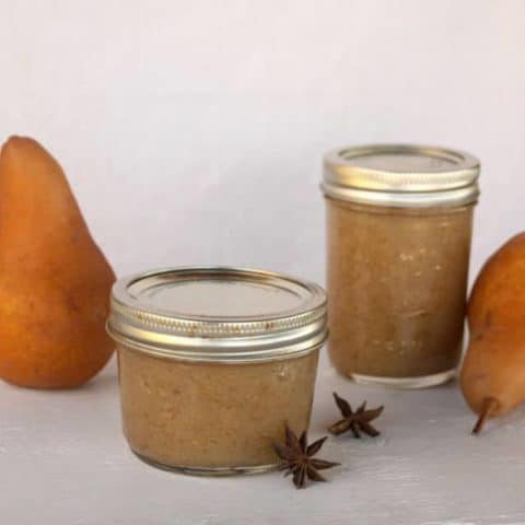 Jars of pear butter with whole pears and spices.