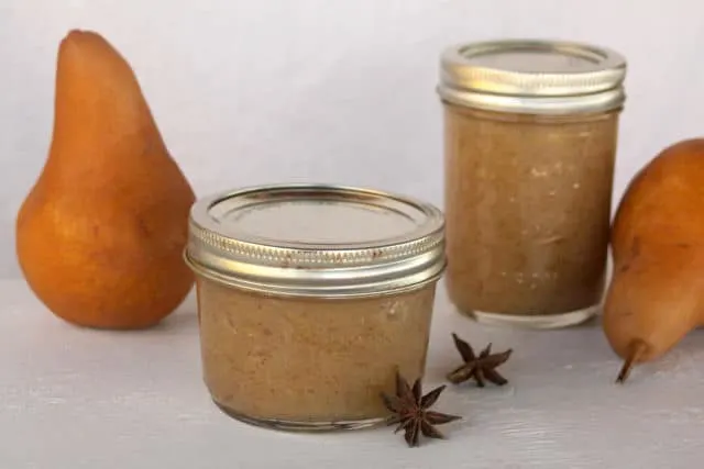 Jars of pear butter with whole pears and spices.