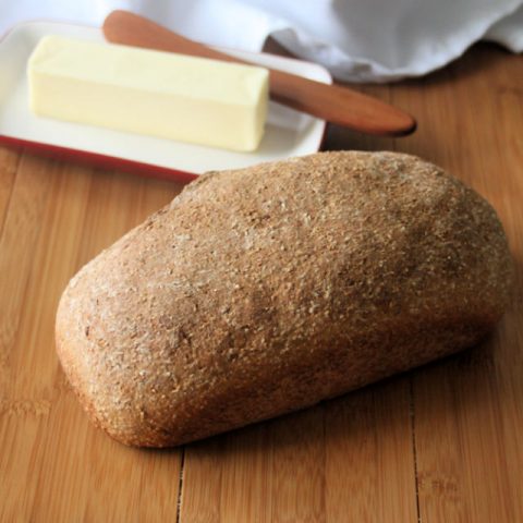 A loaf of garlic herb bread on a board with a stick of butter.