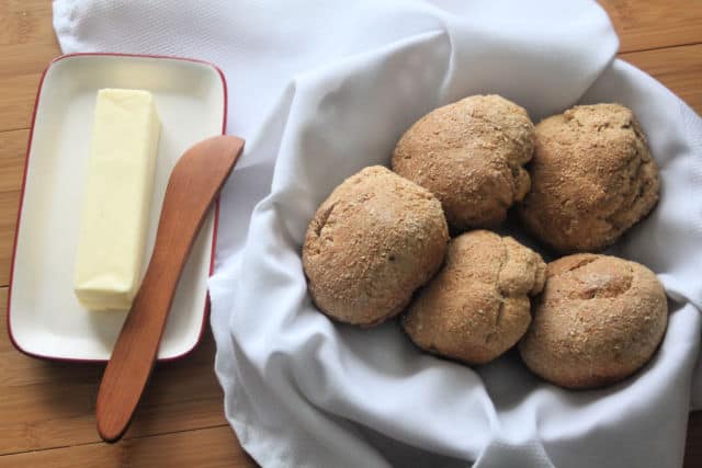 Garlic herb rolls in a linen lined basket with a stick of butter and wood spreader.