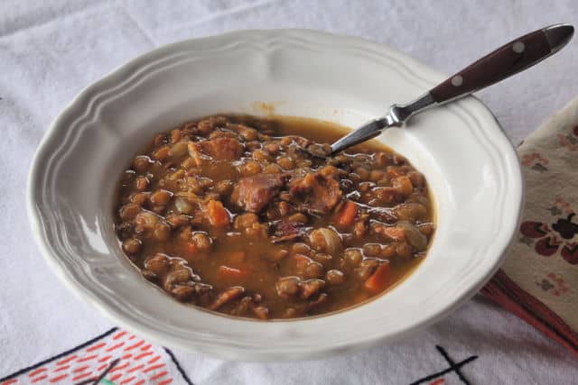 A bowl of lentil bacon soup on a tablecloth.