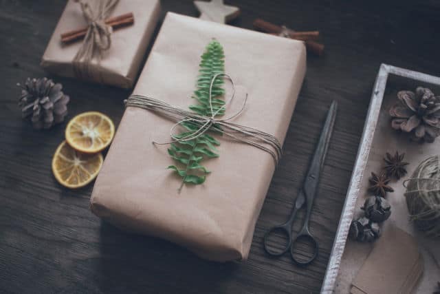 A gift wrapped in brown paper with a leaf and twine surrounded by dried fruit and spices.