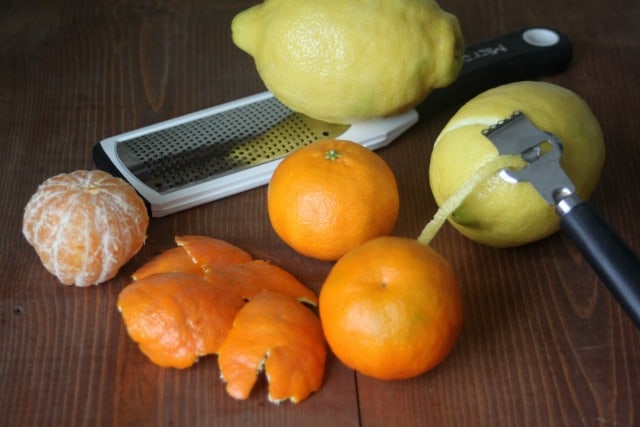 A variety of citrus fruit and their peels on a table with zesters.