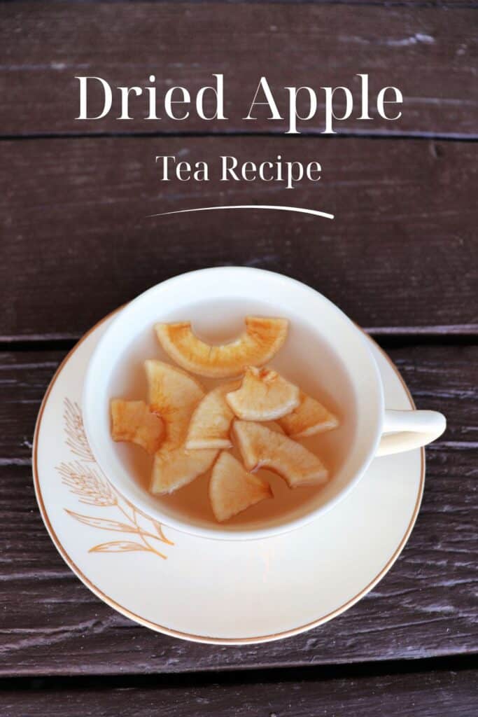 A teacup sits on a saucer. Inside the teacup is hot water with dried apple slices floating on top. Text overlay reads: Dried Apple Tea Recipe. 