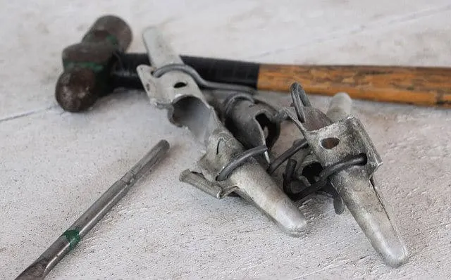 A collection of metal spiles, a hammer, and drill bit used in backyard tree tapping