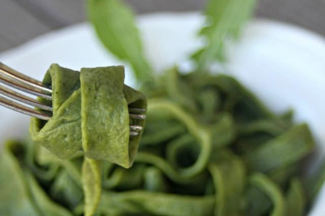 A dandelion egg noodle wrapped around a fork with a bowl of noodles in the background.