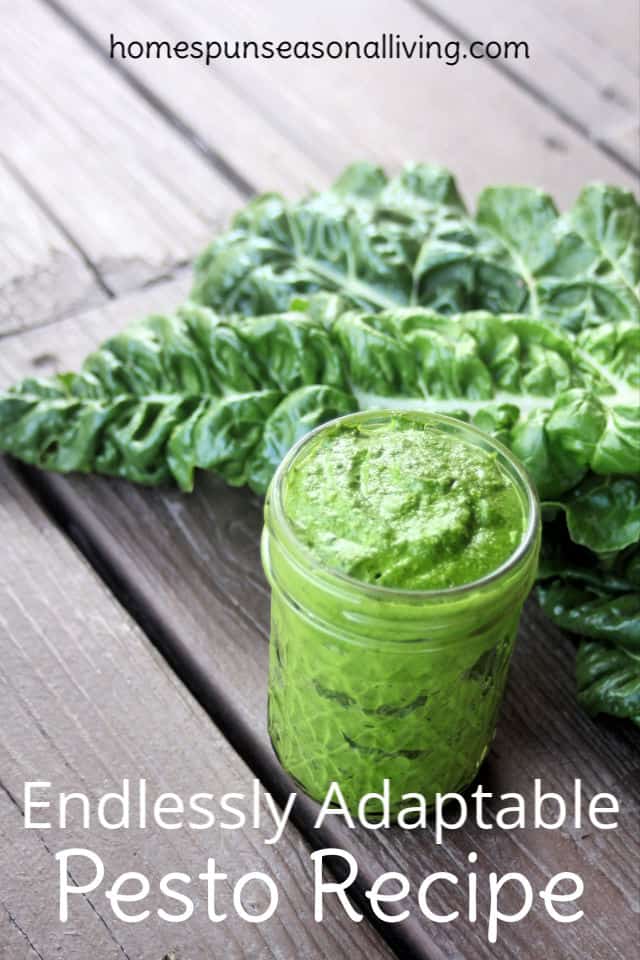 A jar of pesto sitting on a table in front of chard leaves.