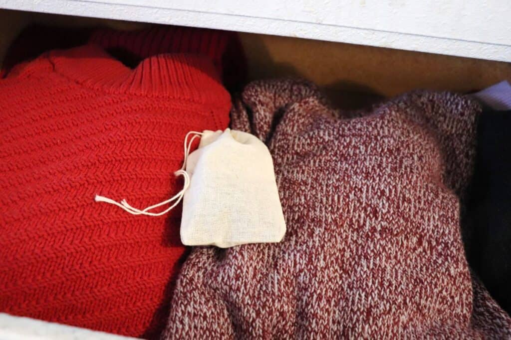 A small cloth bag of herbal moth repellant sits on top of red sweaters in an open draw. 