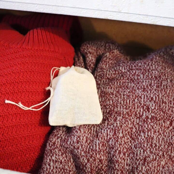 A cloth bag of herbal moth repellent sits on top of red sweaters in an open drawer.