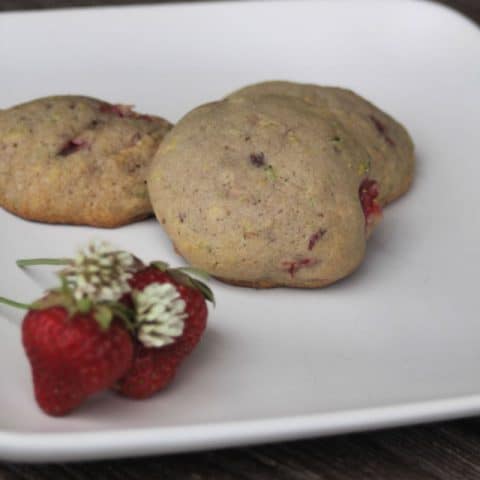 3 strawberry white clover cookies on a plate with fresh strawberries and white clover blossoms.