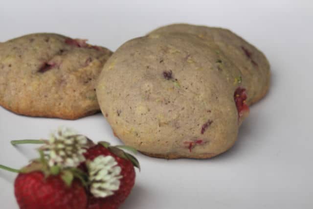 3 strawberry white clover cookies on a plate with fresh strawberries and white clover blossoms.