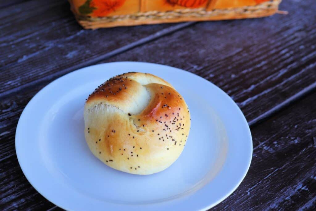 A roll with poppy seeds on top sits on a white plate. 