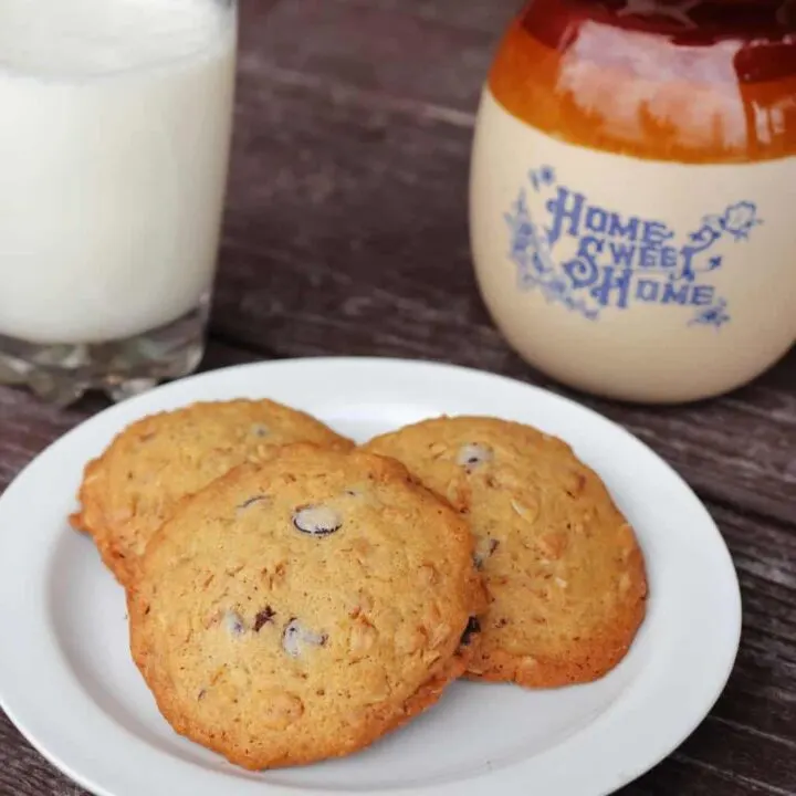 3 cookies on a white plate. A glass of milk and earthenware pitcher with the words 'home sweet home' on it sit in the background.