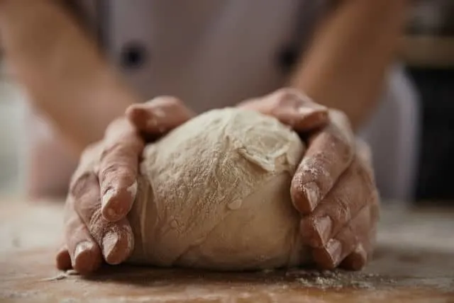 Hands kneading bread dough on a board.