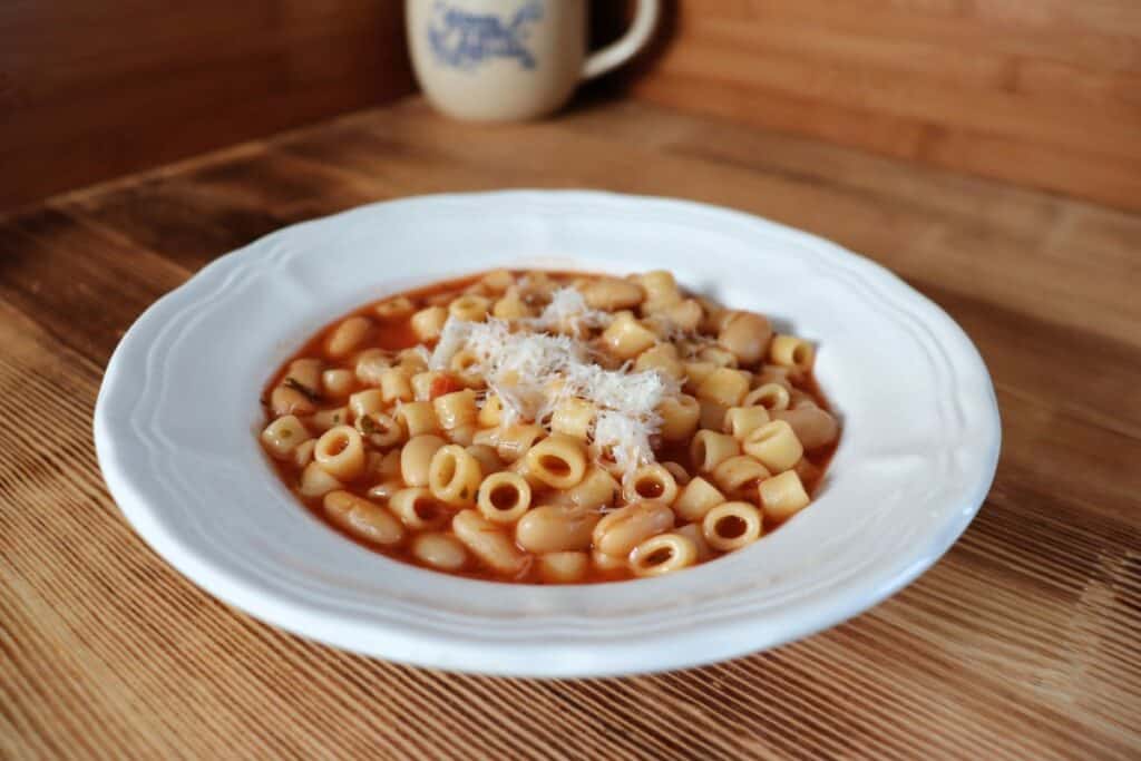 A parmesan cheese topped bowl of pasta e fagioli sits on a table. 