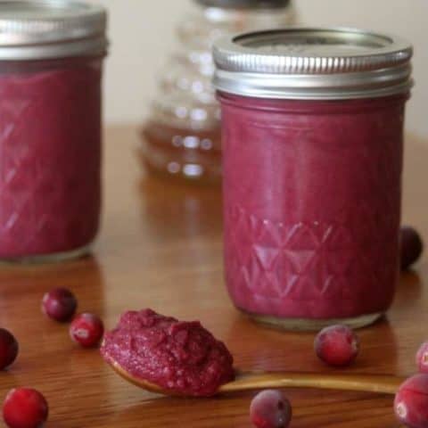 Jars of cranberry honey mustard on a table with some sitting on a spoon.