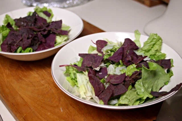 Two bowls full of leafy green salads on a wooden board.
