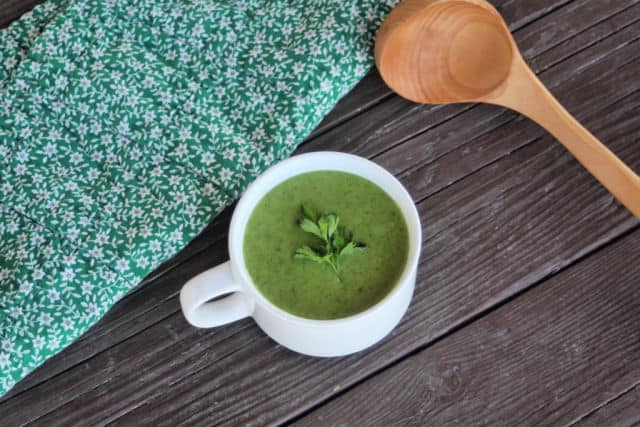 A bowl of green soup with a napkin and wooden ladle.