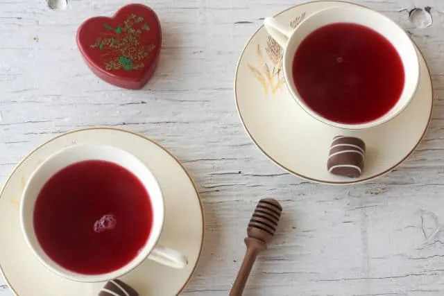 Two cups of hibcus tea in cups on saucers with chocolate candies.