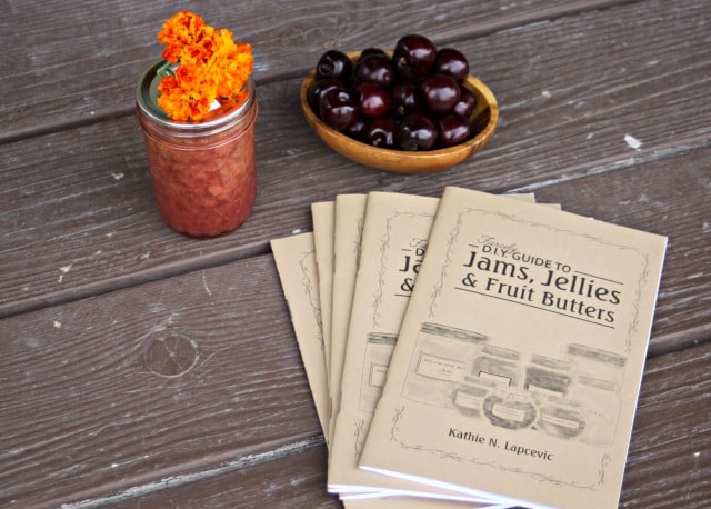 Copies of a jams guide booklet sitting in front of a jar of jam and bowl of cherries.