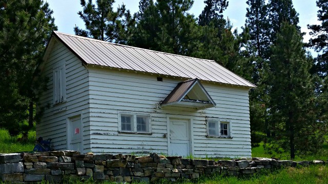 An old white sided home on a hill.