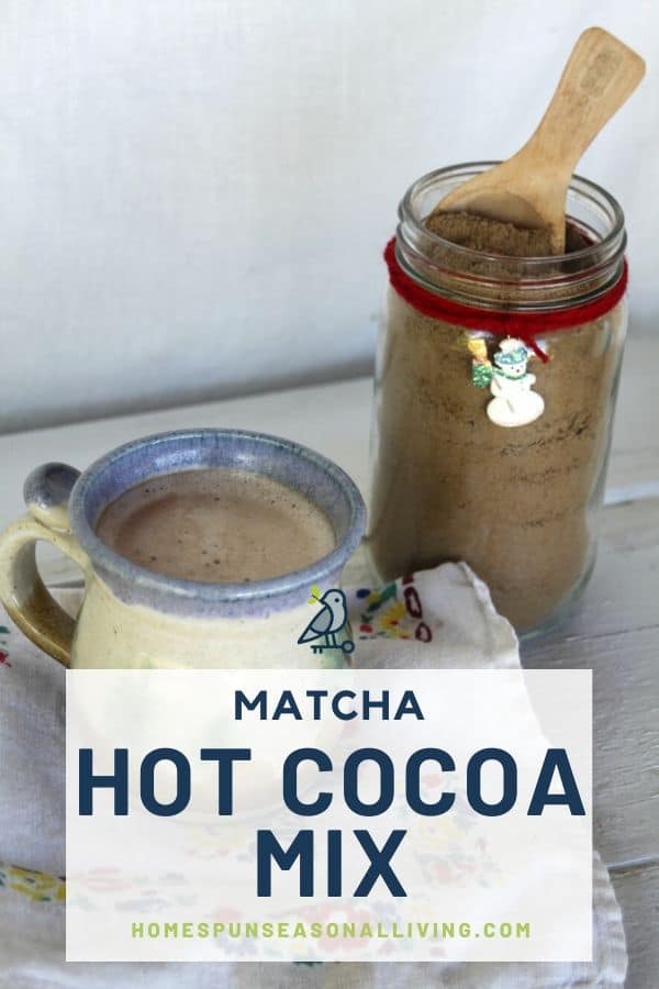 A jar of matcha hot cocoa mix with a wooden spoon in it sitting in front of a cup of hot cocoa. 