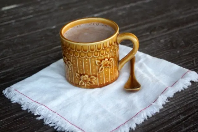 A cup of hot cocoa with a spoon on a cloth napkin.