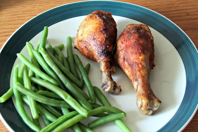 2 chicken legs on a dinner plate with green beans.