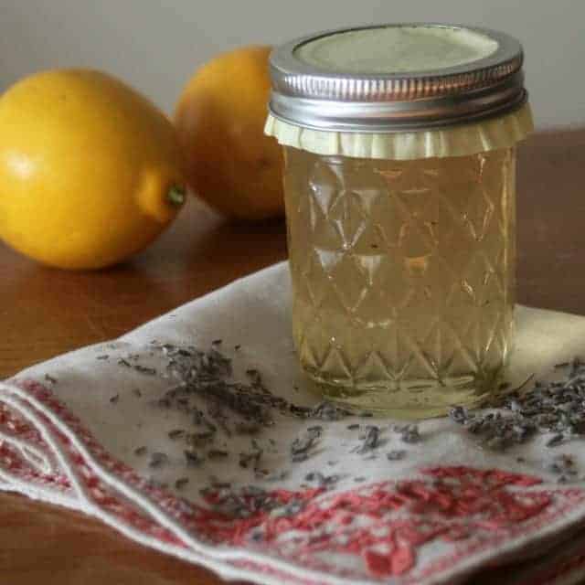 A jar of lemon lavender jelly sitting on a napkin with lemons in the background.